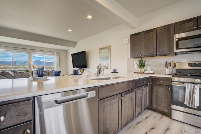 kitchen featuring beam ceiling, a sink, tasteful backsplash, stainless steel appliances, and dark brown cabinetry