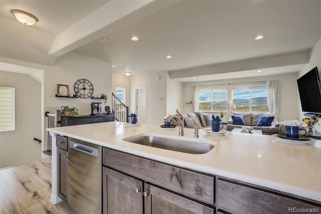 kitchen featuring a sink, open floor plan, light wood finished floors, dishwasher, and light countertops