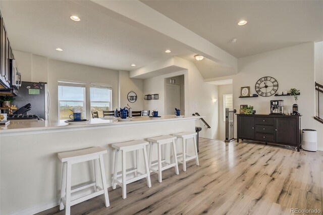 kitchen featuring a breakfast bar, a peninsula, recessed lighting, freestanding refrigerator, and light wood-style floors