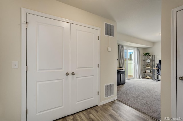 hallway with carpet, wood finished floors, and visible vents