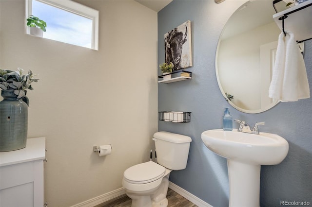 half bathroom with a sink, toilet, baseboards, and wood finished floors