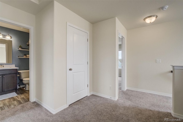 hallway featuring light colored carpet, baseboards, and a sink