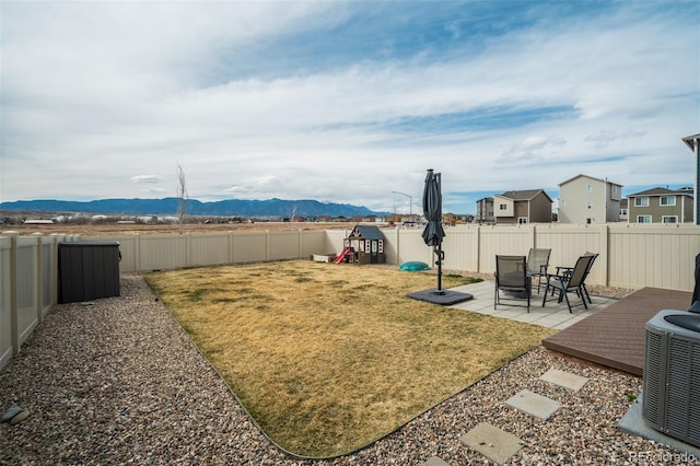 view of yard featuring a playground, central AC unit, a fenced backyard, a patio area, and a mountain view