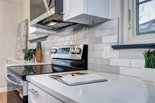 kitchen with stainless steel electric stove, light countertops, white cabinets, backsplash, and wood finished floors