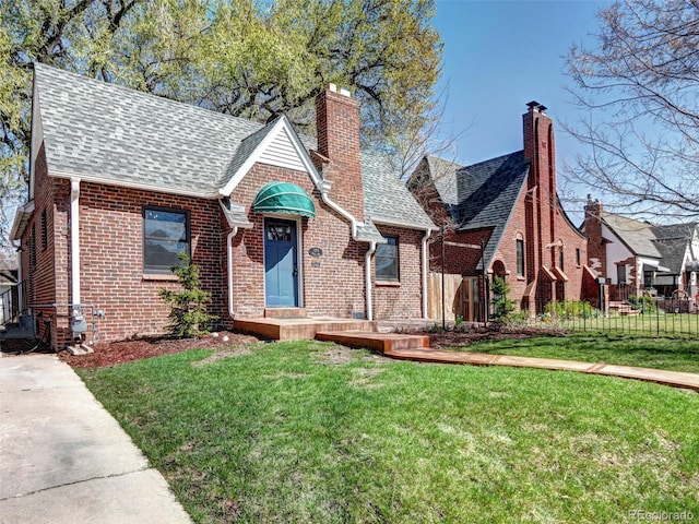 english style home featuring brick siding, roof with shingles, and a chimney