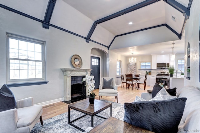 living room featuring arched walkways, lofted ceiling, baseboards, a fireplace, and light wood-style floors