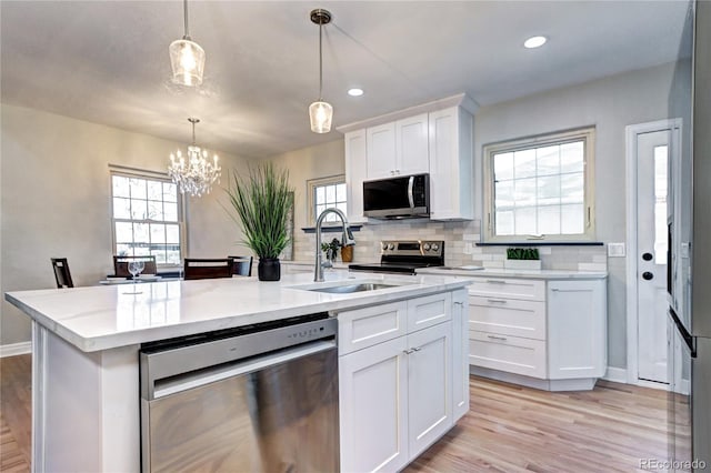 kitchen with appliances with stainless steel finishes, a sink, a chandelier, white cabinets, and light wood-style flooring