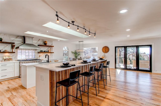 kitchen with an island with sink, tasteful backsplash, wall chimney exhaust hood, white cabinets, and sink