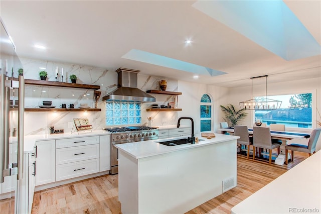 kitchen featuring high end stove, backsplash, wall chimney exhaust hood, white cabinets, and sink