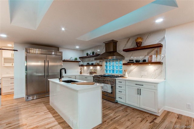 kitchen featuring backsplash, a center island with sink, sink, high end appliances, and ventilation hood