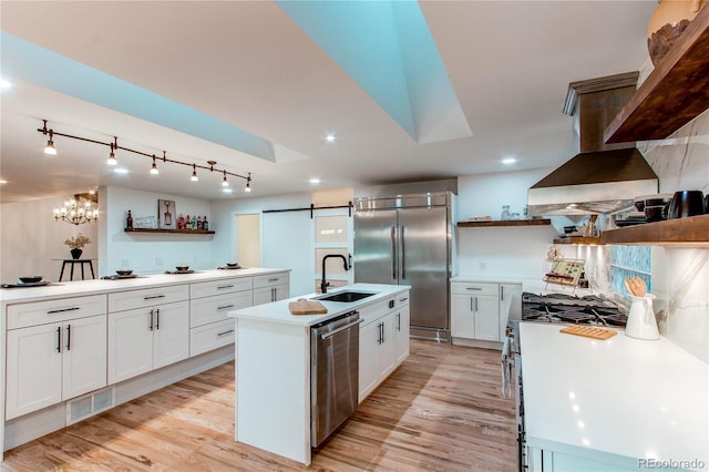 kitchen featuring white cabinets, appliances with stainless steel finishes, sink, a center island with sink, and a barn door