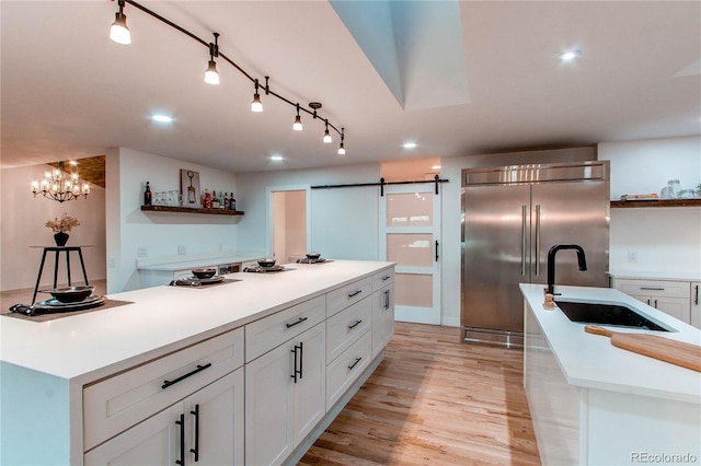 kitchen featuring an island with sink, white cabinets, stainless steel built in fridge, and sink