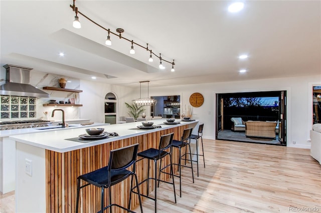 kitchen featuring extractor fan, tasteful backsplash, an island with sink, sink, and a kitchen breakfast bar