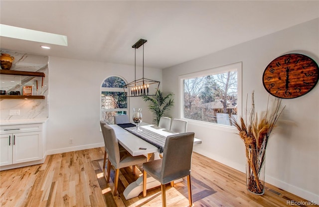 dining room featuring a skylight, light hardwood / wood-style floors, and a notable chandelier