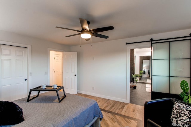 bedroom featuring ceiling fan, a barn door, and hardwood / wood-style flooring