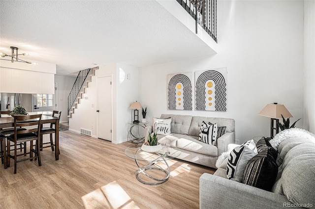 living area with stairway, light wood-style flooring, baseboards, a notable chandelier, and visible vents