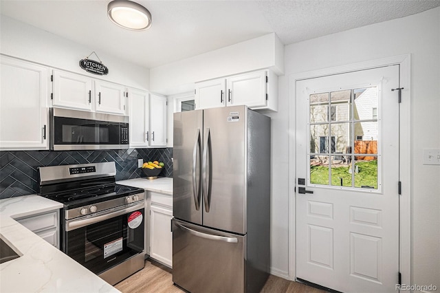kitchen with white cabinets, light stone countertops, decorative backsplash, light wood-style flooring, and appliances with stainless steel finishes