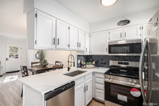 kitchen featuring a sink, tasteful backsplash, white cabinetry, light stone countertops, and appliances with stainless steel finishes