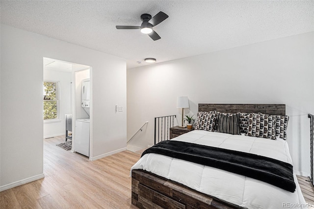 bedroom featuring baseboards, stacked washing maching and dryer, a textured ceiling, and light wood-type flooring