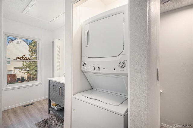clothes washing area with attic access, light wood-type flooring, baseboards, stacked washer and dryer, and laundry area