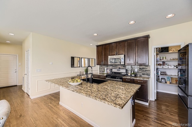 kitchen with appliances with stainless steel finishes, a sink, dark brown cabinets, light stone countertops, and recessed lighting