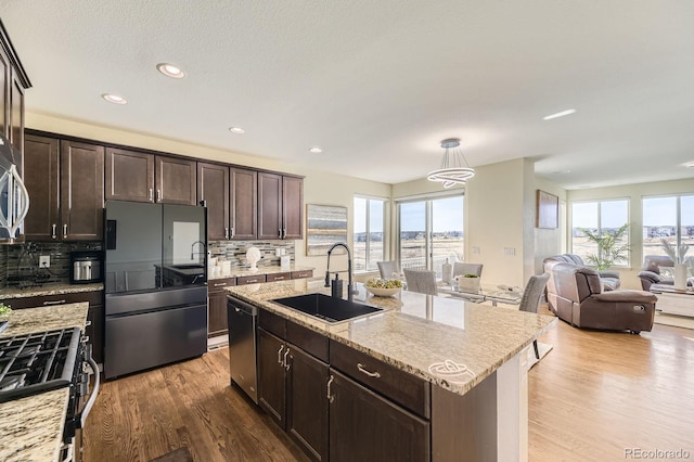 kitchen featuring stainless steel appliances, a sink, wood finished floors, decorative backsplash, and dark brown cabinetry