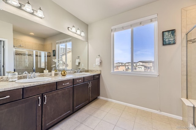 bathroom featuring a shower stall, double vanity, baseboards, and tile patterned flooring