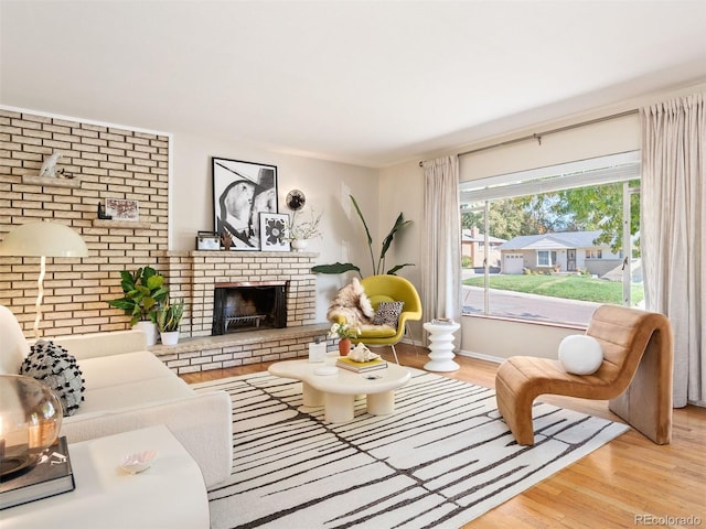 living room featuring brick wall, a fireplace, and light hardwood / wood-style flooring