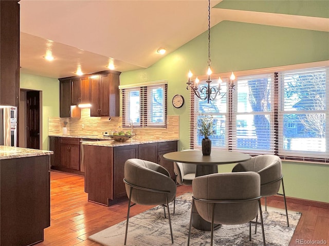 kitchen with vaulted ceiling, a chandelier, decorative light fixtures, light hardwood / wood-style floors, and backsplash