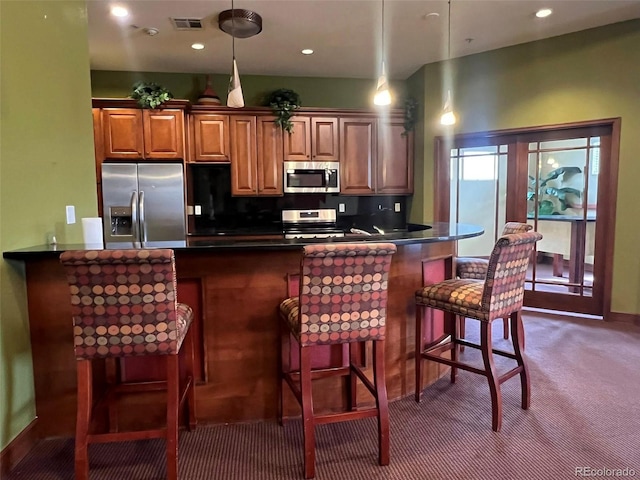 kitchen with decorative backsplash, a breakfast bar area, stainless steel appliances, dark colored carpet, and visible vents