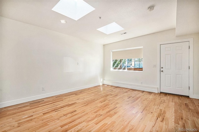 spare room with a skylight and light hardwood / wood-style floors