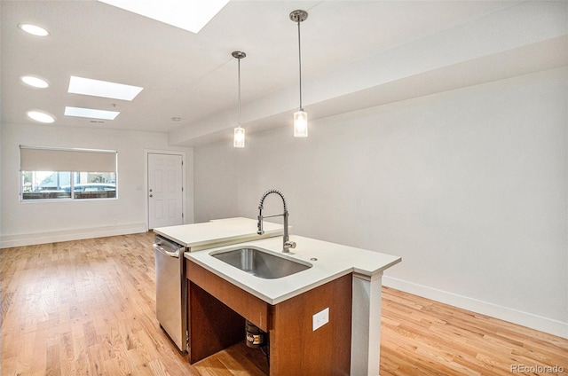 kitchen with a skylight, stainless steel dishwasher, decorative light fixtures, a center island with sink, and light hardwood / wood-style floors