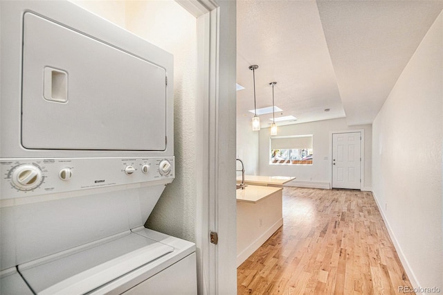 washroom with light hardwood / wood-style floors and stacked washer / drying machine