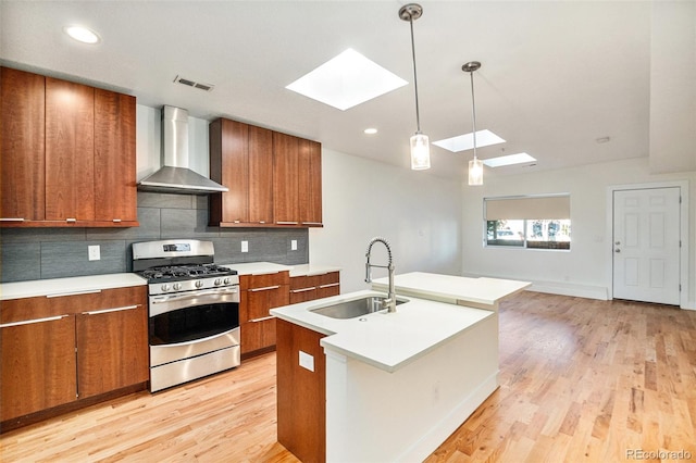 kitchen with light wood-type flooring, sink, wall chimney range hood, a skylight, and gas range