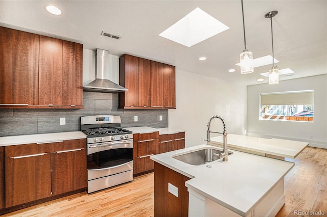 kitchen with light wood-type flooring, sink, stainless steel gas range, wall chimney range hood, and a skylight