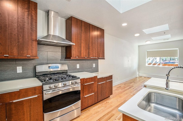 kitchen featuring light wood-type flooring, sink, wall chimney range hood, stainless steel gas stove, and a skylight