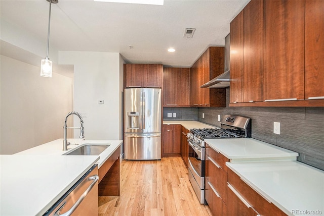 kitchen with decorative light fixtures, wall chimney range hood, appliances with stainless steel finishes, light hardwood / wood-style floors, and decorative backsplash