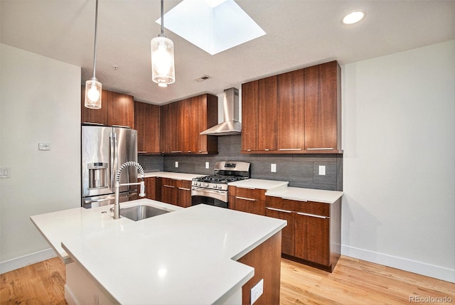 kitchen featuring wall chimney exhaust hood, a center island with sink, appliances with stainless steel finishes, and a skylight