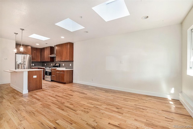 kitchen with pendant lighting, a skylight, a kitchen island, appliances with stainless steel finishes, and light wood-type flooring