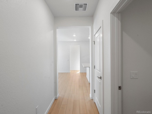 hallway with visible vents, light wood-style flooring, and baseboards