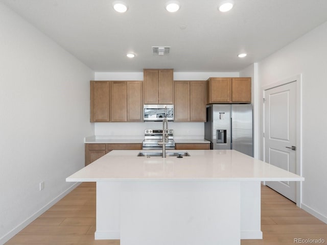 kitchen featuring a center island with sink, light countertops, visible vents, appliances with stainless steel finishes, and brown cabinetry