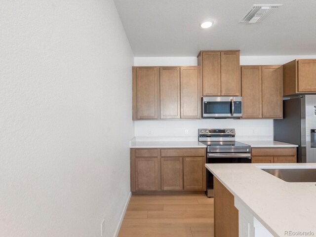 kitchen with light wood finished floors, visible vents, brown cabinets, stainless steel appliances, and light countertops