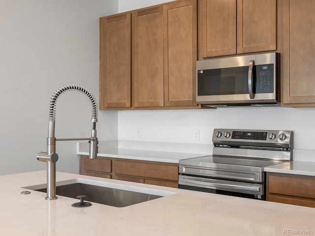 kitchen with appliances with stainless steel finishes, brown cabinets, light countertops, and a sink