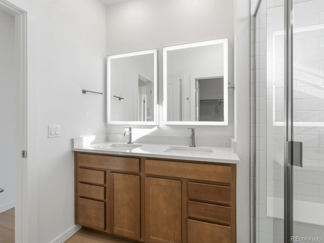 full bathroom featuring baseboards, double vanity, a sink, and a shower stall