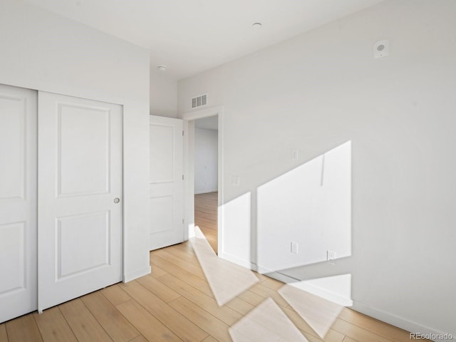 unfurnished bedroom featuring light wood-type flooring, a closet, visible vents, and baseboards