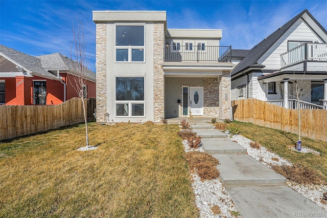 view of front of house featuring stucco siding, a front yard, a balcony, and fence