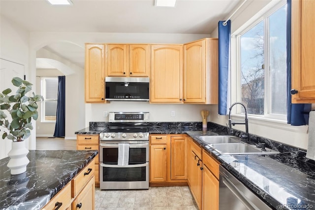 4844 Mt Evans St, Brighton, CO 80601 - kitchen with stainless steel appliances, a sink, arched walkways, light brown cabinetry, and dark stone countertops