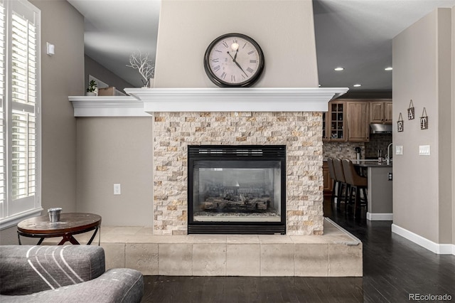 room details with tasteful backsplash, a glass covered fireplace, wood finished floors, under cabinet range hood, and baseboards