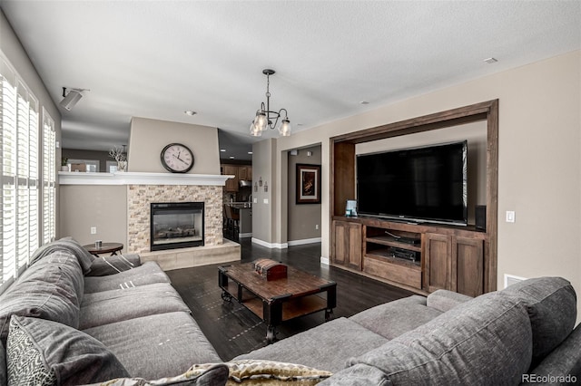 living room featuring dark wood-type flooring, a glass covered fireplace, a textured ceiling, and baseboards