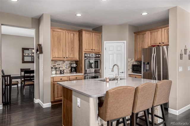 kitchen with stainless steel appliances, light countertops, a sink, and a kitchen bar